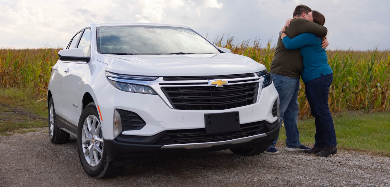 A mother and son hugging while standing next to their Chevy vehicle.