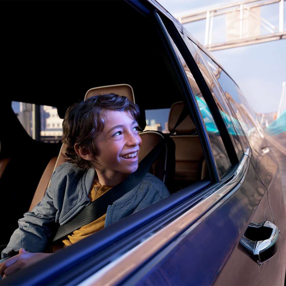 A young boy smiling while looking out the open window of a moving vehicle