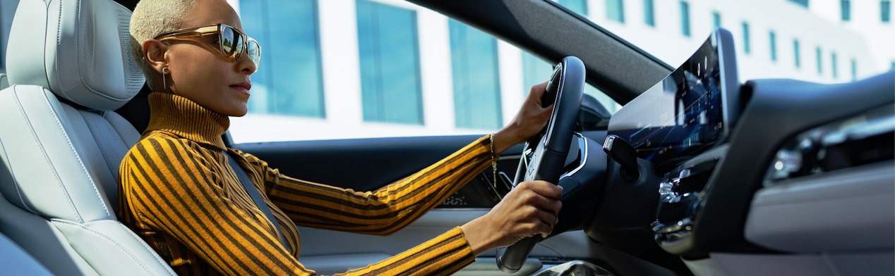 Side view of a woman driving with sunglasses on.