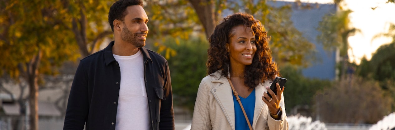 Couple Walking & Smiling While Woman Checks Her Phone