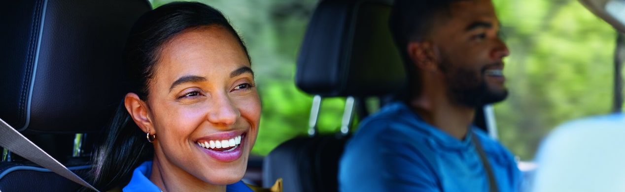 A woman is sitting in the passenger seat of a vehicle who is smiling while looking out the window