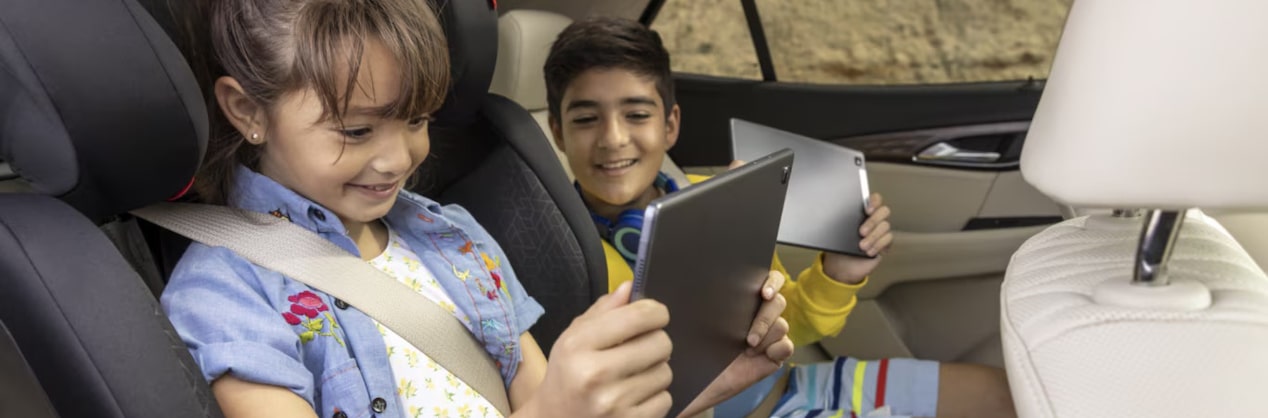 A little girl in a carseat holding a tablet with a little boy sitting next to her who is also looking at the tablet.