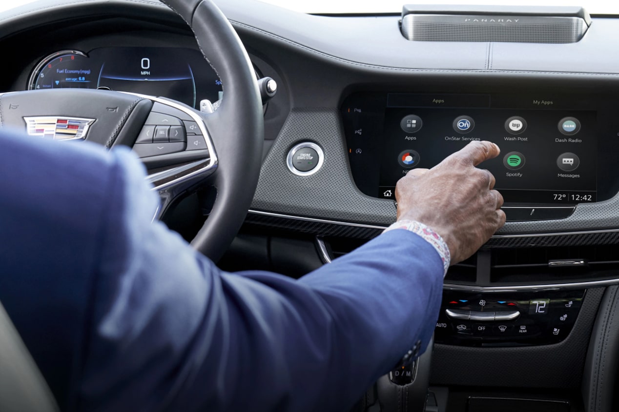 Close-up of a man in the driver's seat of a Cadillac vehicle pressing the display dashboard