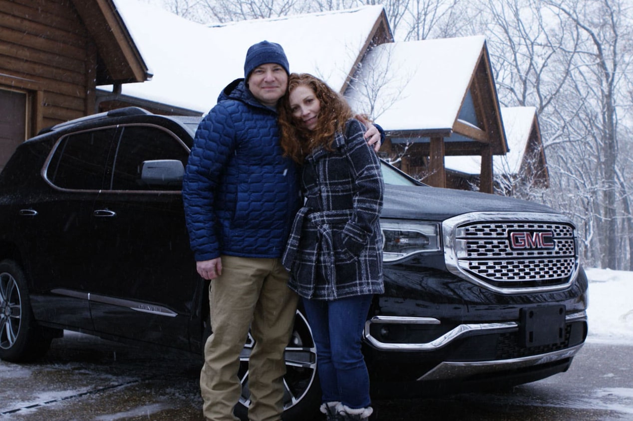 Couple Standing Together in Front of GM Vehicle and Snow Covered Cabin