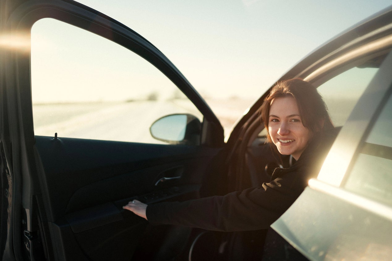 woman sitting in a car with the door open looking back at the camera and smiling