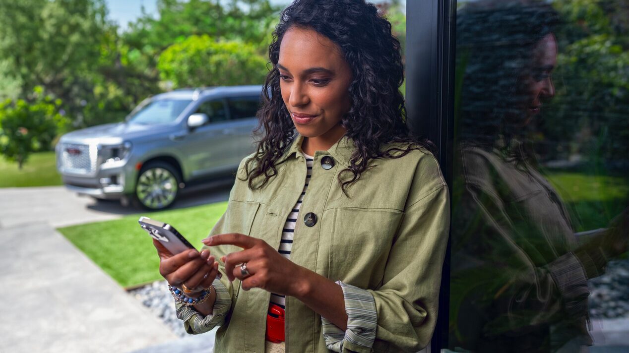 A person stands near a car while looking their smartphone.