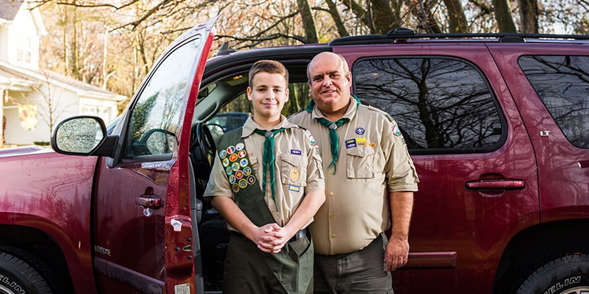 Boy Scout and Scoutmaster Standing Side by Side in Front of GM Vehicle