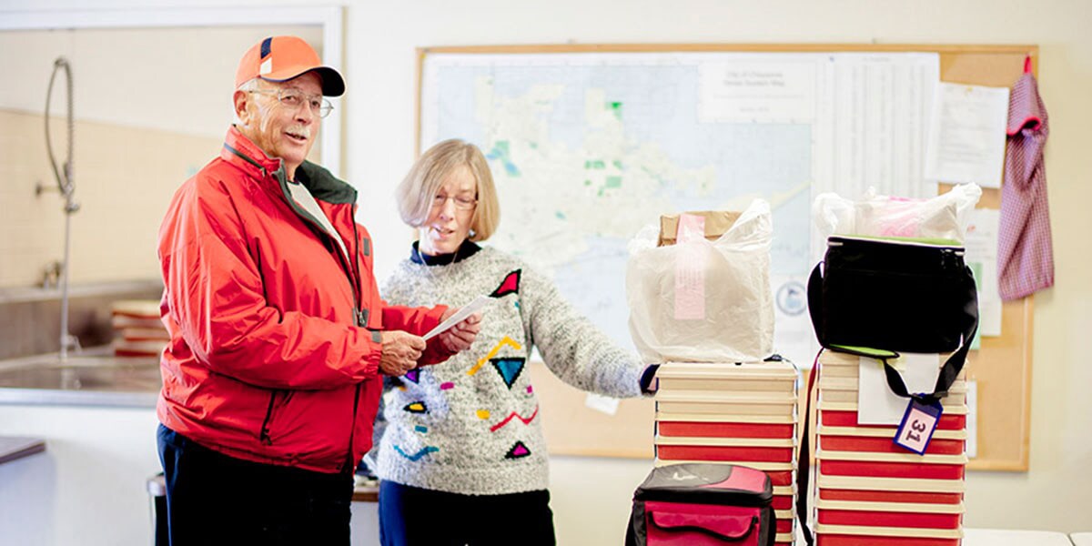 Elderly Couple Standing in Kitchen Next to Luggage 