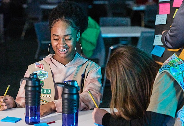 Girl Scouts sitting at a table writing on notepads