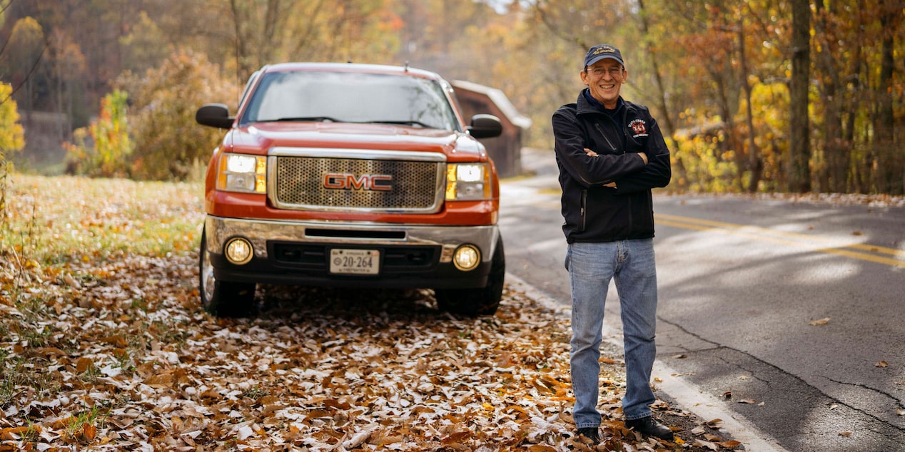 Man Stands In Front of GMC Truck in Fall Landscape