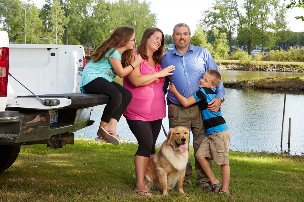 Family of 4 with Their Dog Standing Together at Vehicles Tailgate