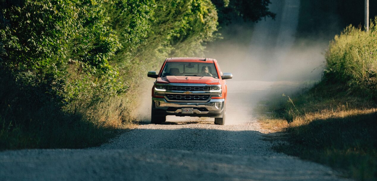 GM Truck Driving Down a Narrow Gravel Road With Dust Kicking Up