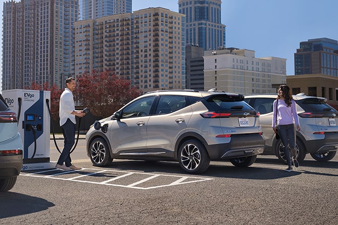 Man Begins to Charge Electric Chevy While Woman Walks Behind It