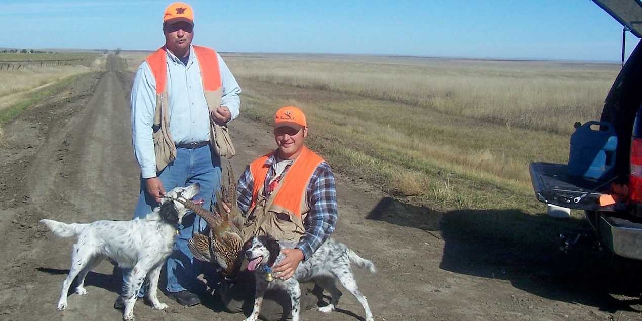 Two Men Posing in a Field with Their Dogs