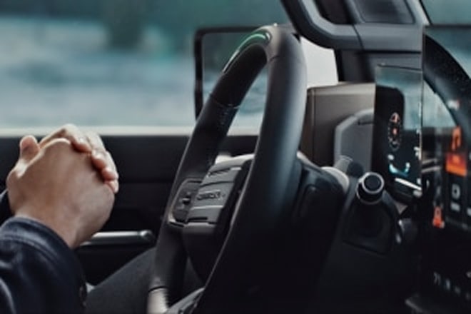 A person's hands clapsed together in front of the steering wheel.
