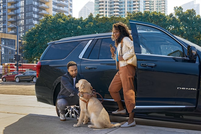 A Couple and Their Dog Standing Next to GM Vehicle