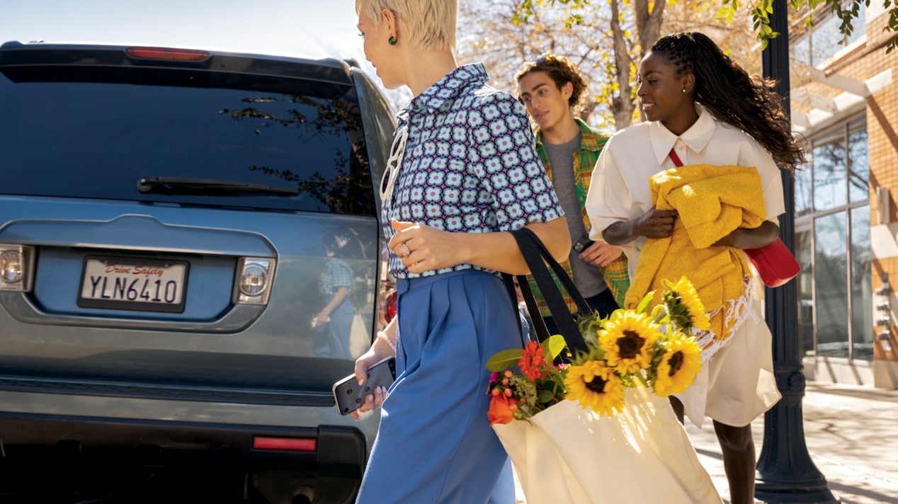 Three People Walk Around GM Vehicle Parked on Street