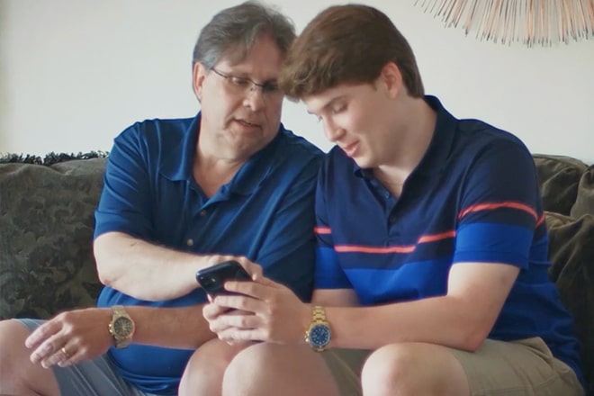 Father and Son Sit Together Looking at Smartphone