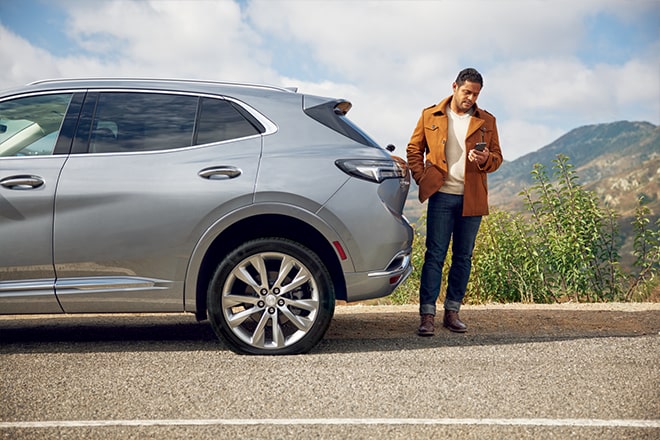 Man Stands at the Rear of His Buick Checking His Phone