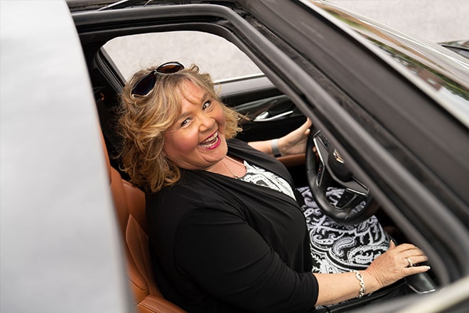 A woman smiling up at a camera through her vehicles sunroof 