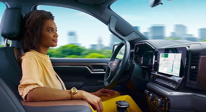 A woman is in the driver seat of a vehicle and has her right arm resting on the center console.