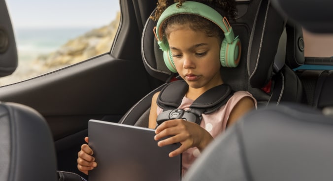 Little Girl in a Car Seat Using an iPad with Headphones